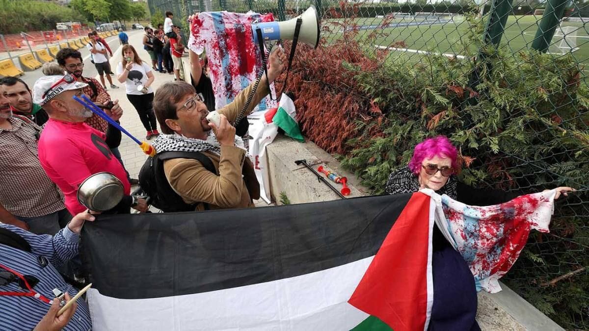 Manifestantes de la campaña #ArgentinaNoVayas sostienen una camiseta argentina manchada con pintura roja frente al predio de entrenamiento de la selección en Barcelona, antes de la suspensión del amistoso entre Argentina e Israel en 2018.